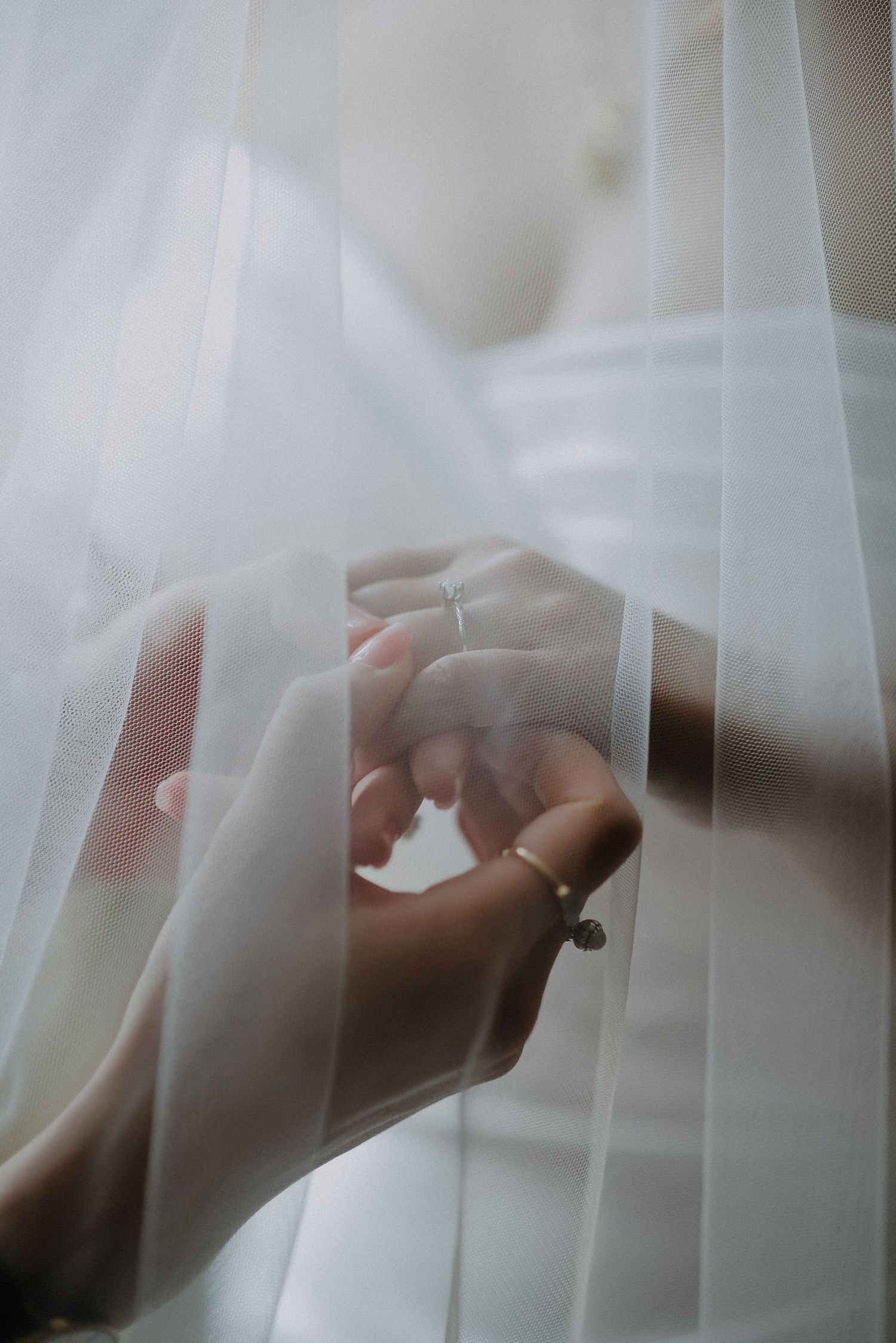 Close-up of hands with wedding rings through delicate white veil fabric.