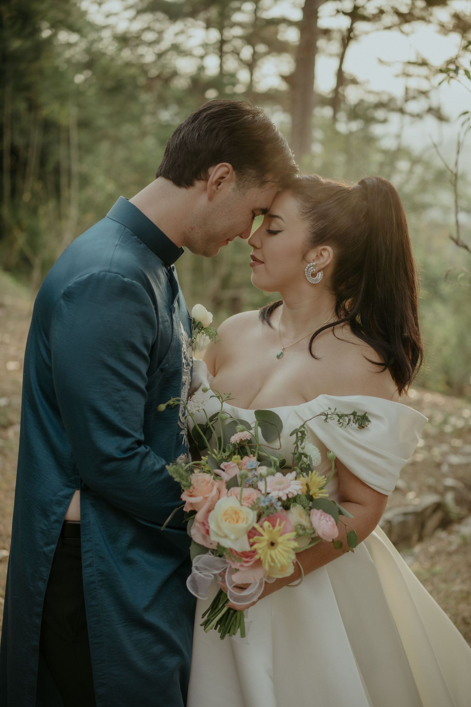A romantic wedding photo showing a newlywed couple in a forest setting with a beautiful floral bouquet.