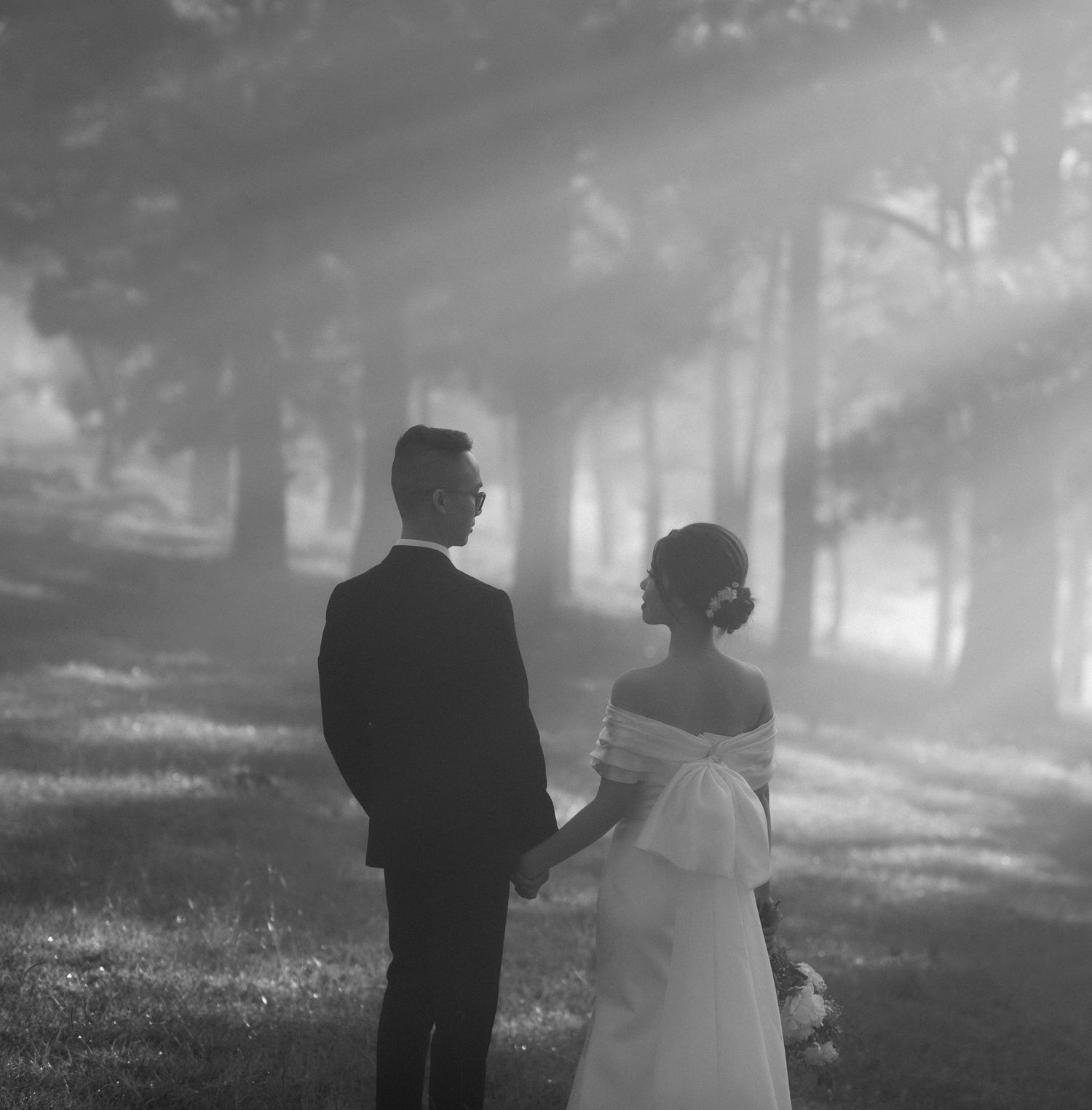 A misty outdoor wedding scene in black and white with a couple holding hands in a dreamy forest setting.