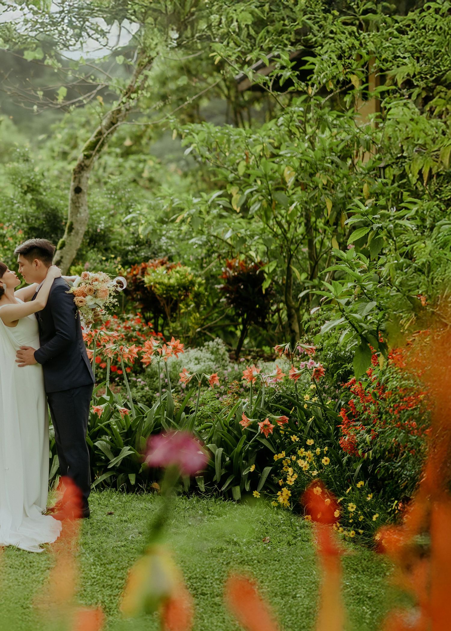 A couple embraces in a lush garden setting with colorful flowers and greenery on a romantic summer day.