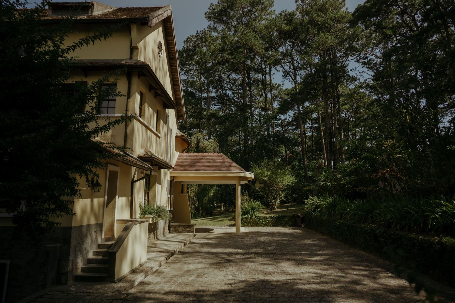 Elegant three-story stucco building with covered walkway surrounded by tall pine trees.