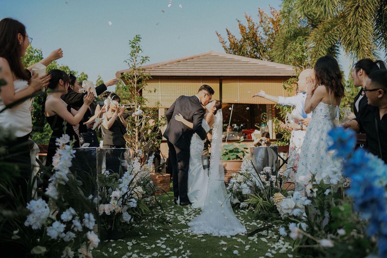 Garden wedding ceremony with couple at gazebo surrounded by white flowers and guests.