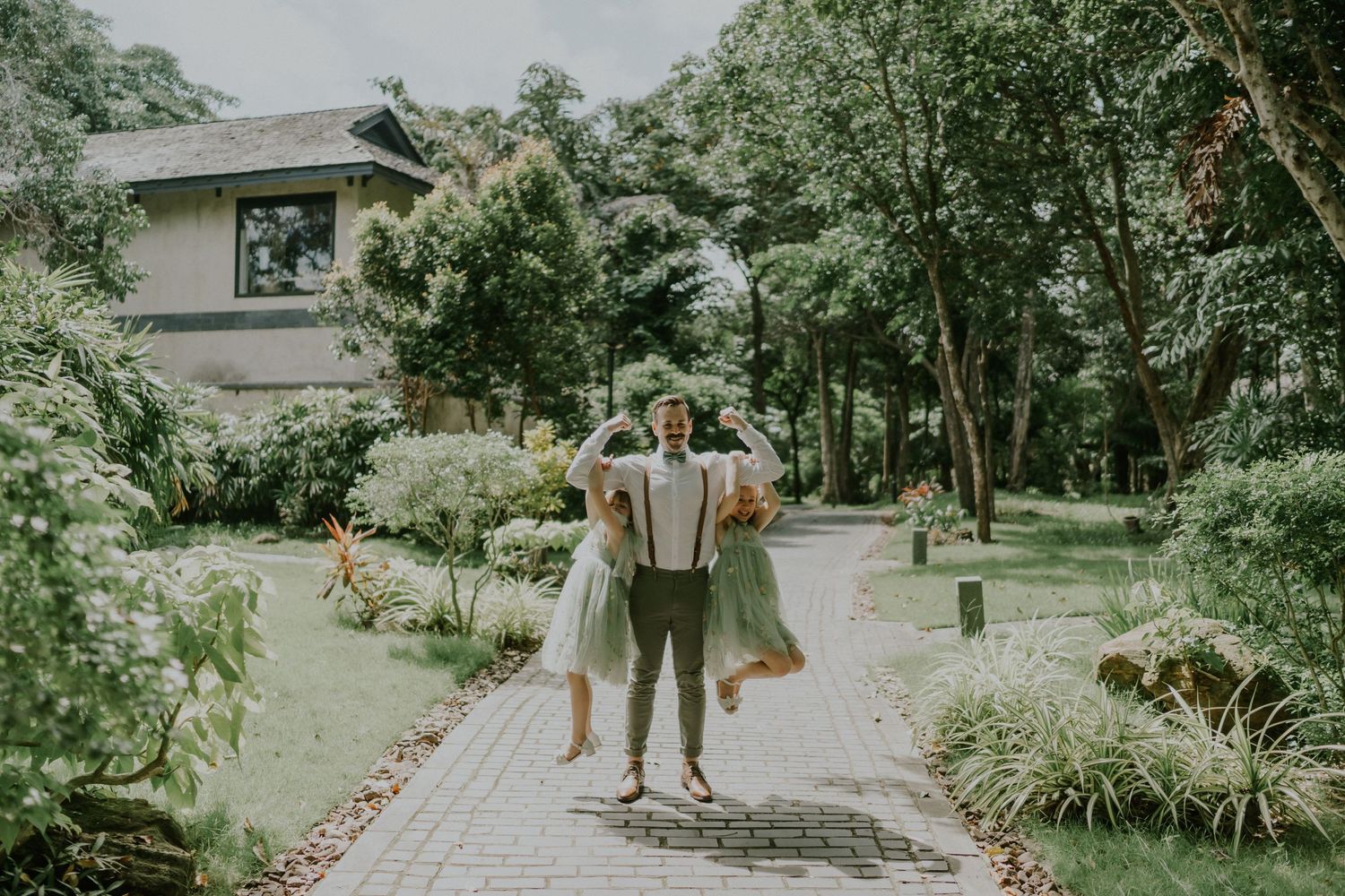 Candid outdoor moment on garden pathway with traditional house in background.