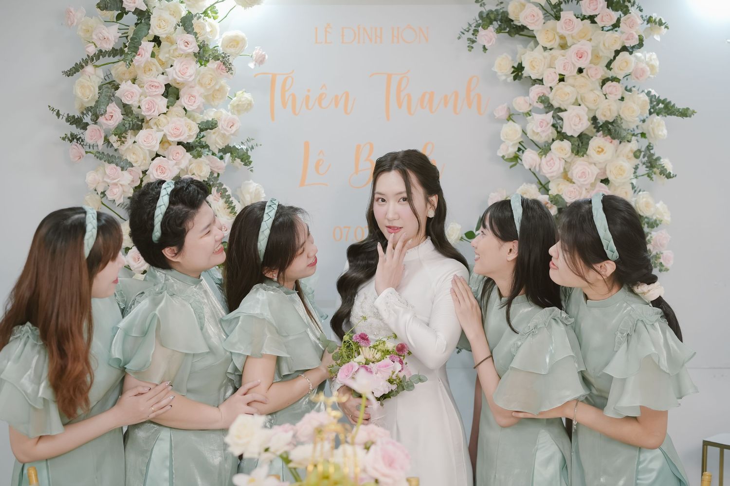 Wedding party scene with bridesmaids in sage green dresses surrounding bride.