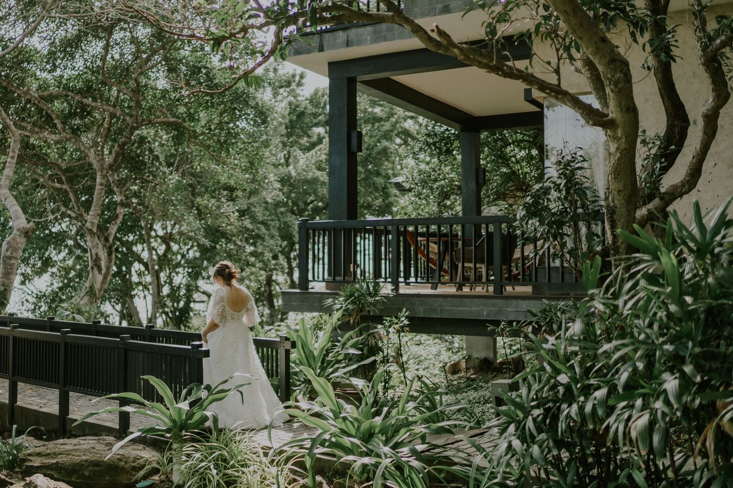 A wedding scene unfolds on a rustic wooden deck surrounded by tropical foliage and trees.