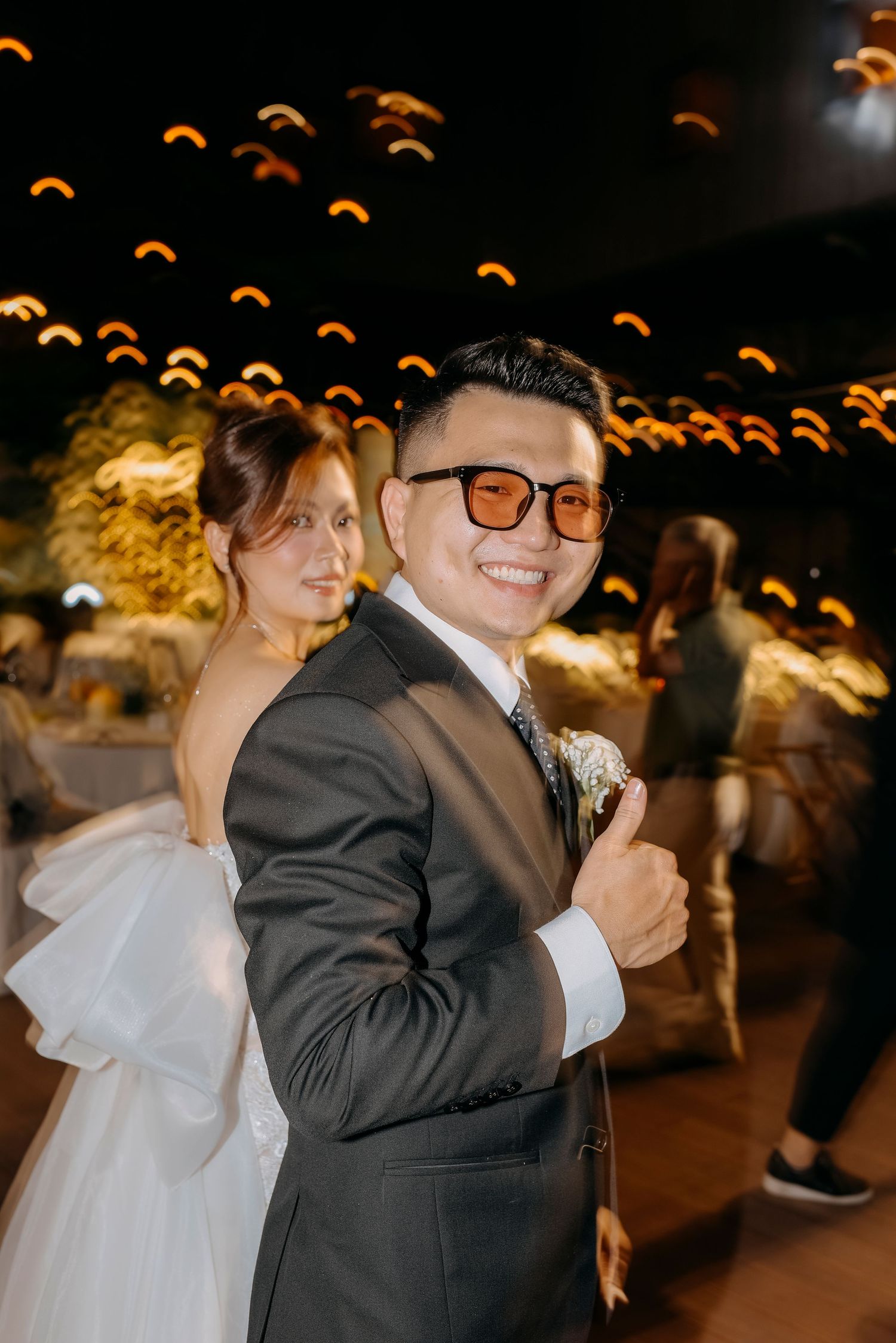 A couple dances beneath warm glowing lights at their wedding reception.