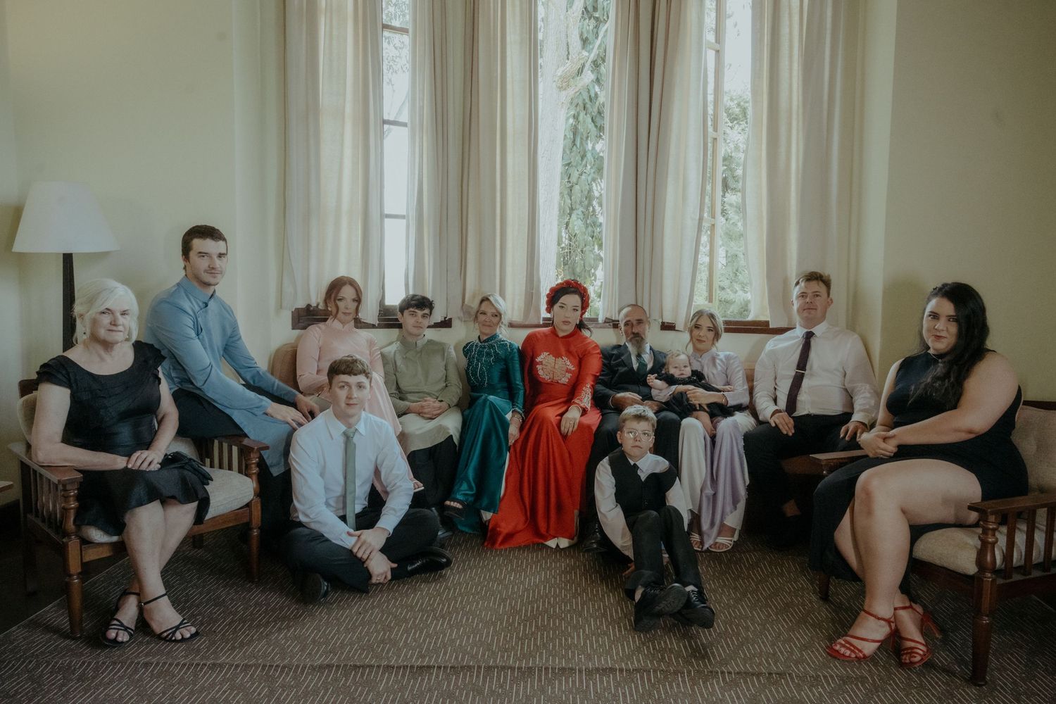 Group of people gathered in a formal setting sitting on furniture, with one person wearing a striking red dress.