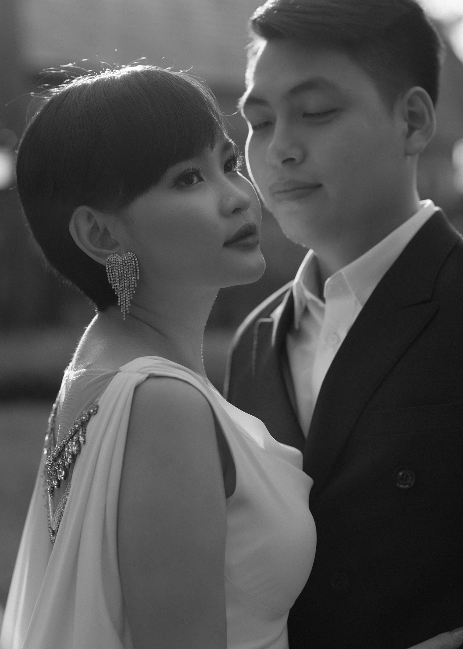 A romantic black and white portrait of a couple in formal attire, with dangling earrings and elegant styling.