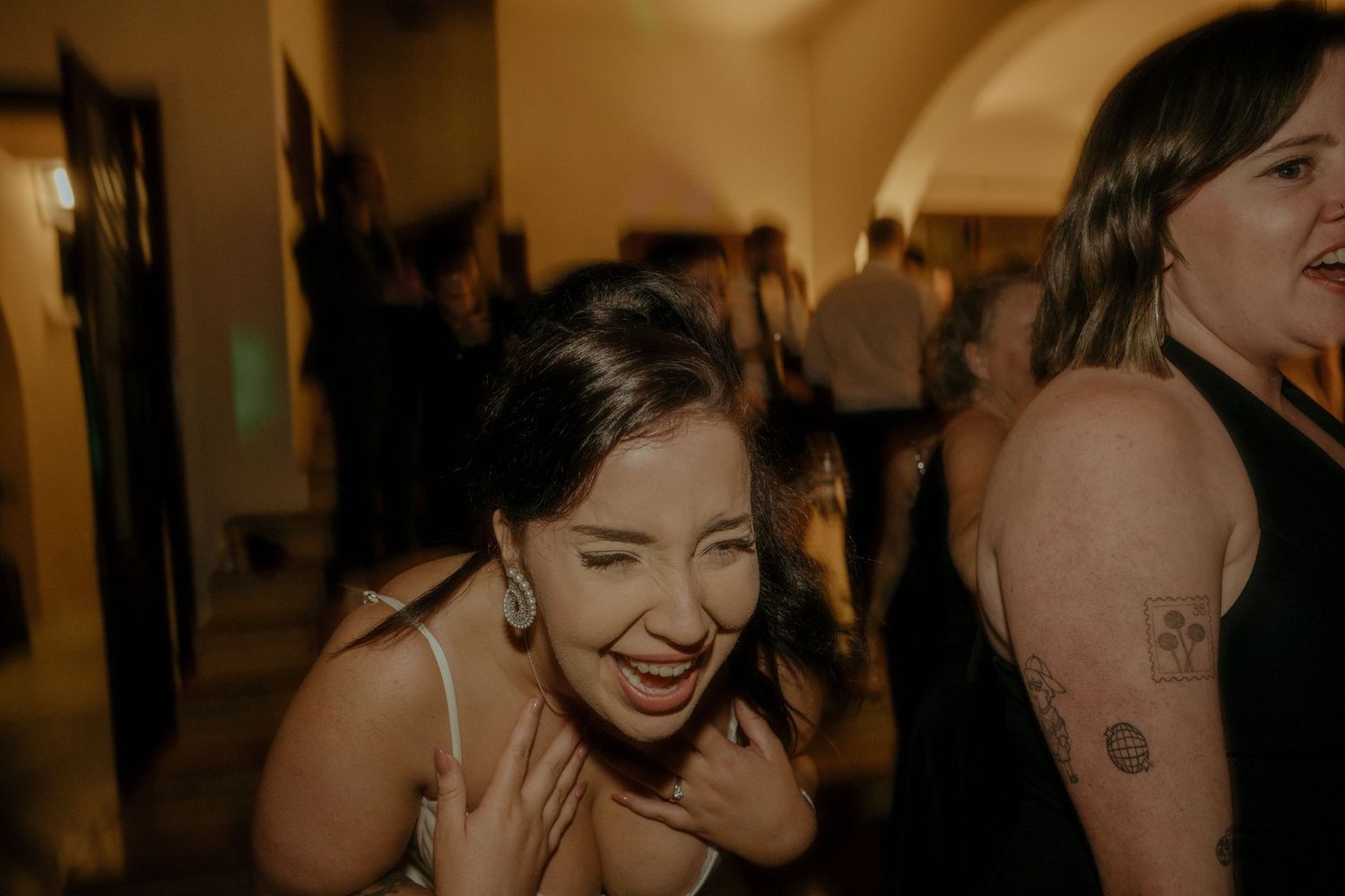 A woman laughs joyfully on a dance floor with warm ambient lighting in the background.
