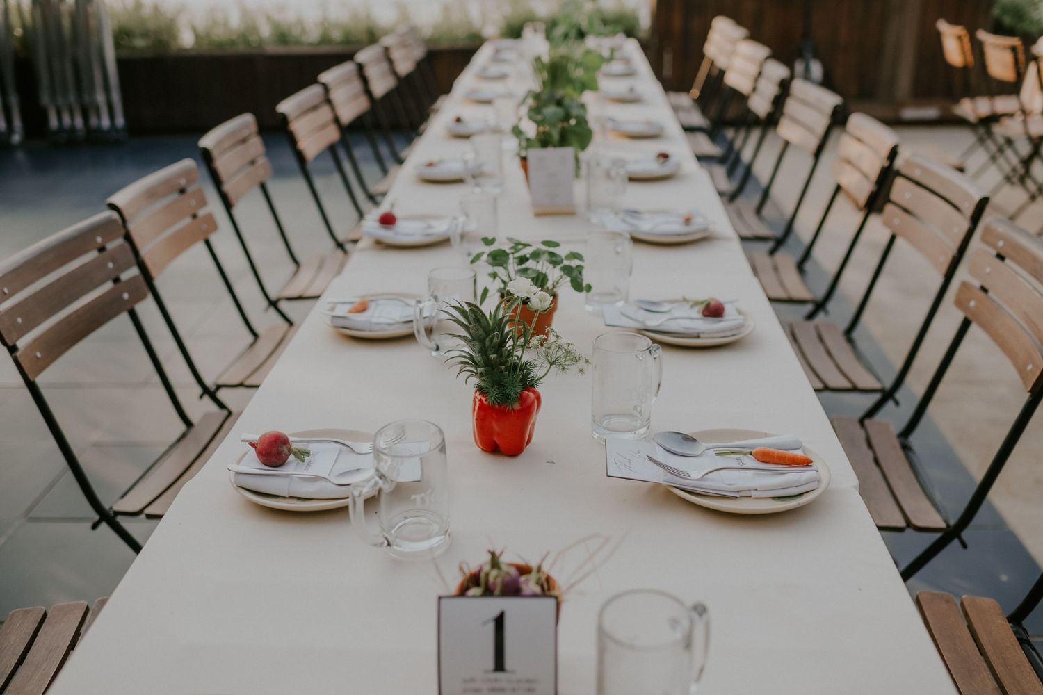 Long banquet table set with white linens and simple place settings for an elegant wedding reception.