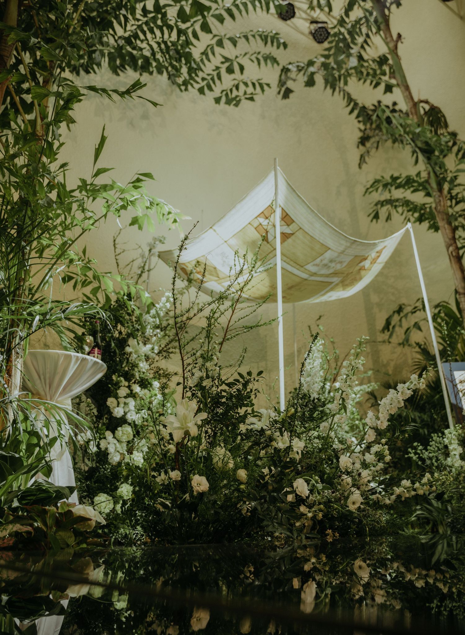 A wedding ceremony setup with white fabric canopy and lush floral arrangements in a romantic garden-inspired setting.