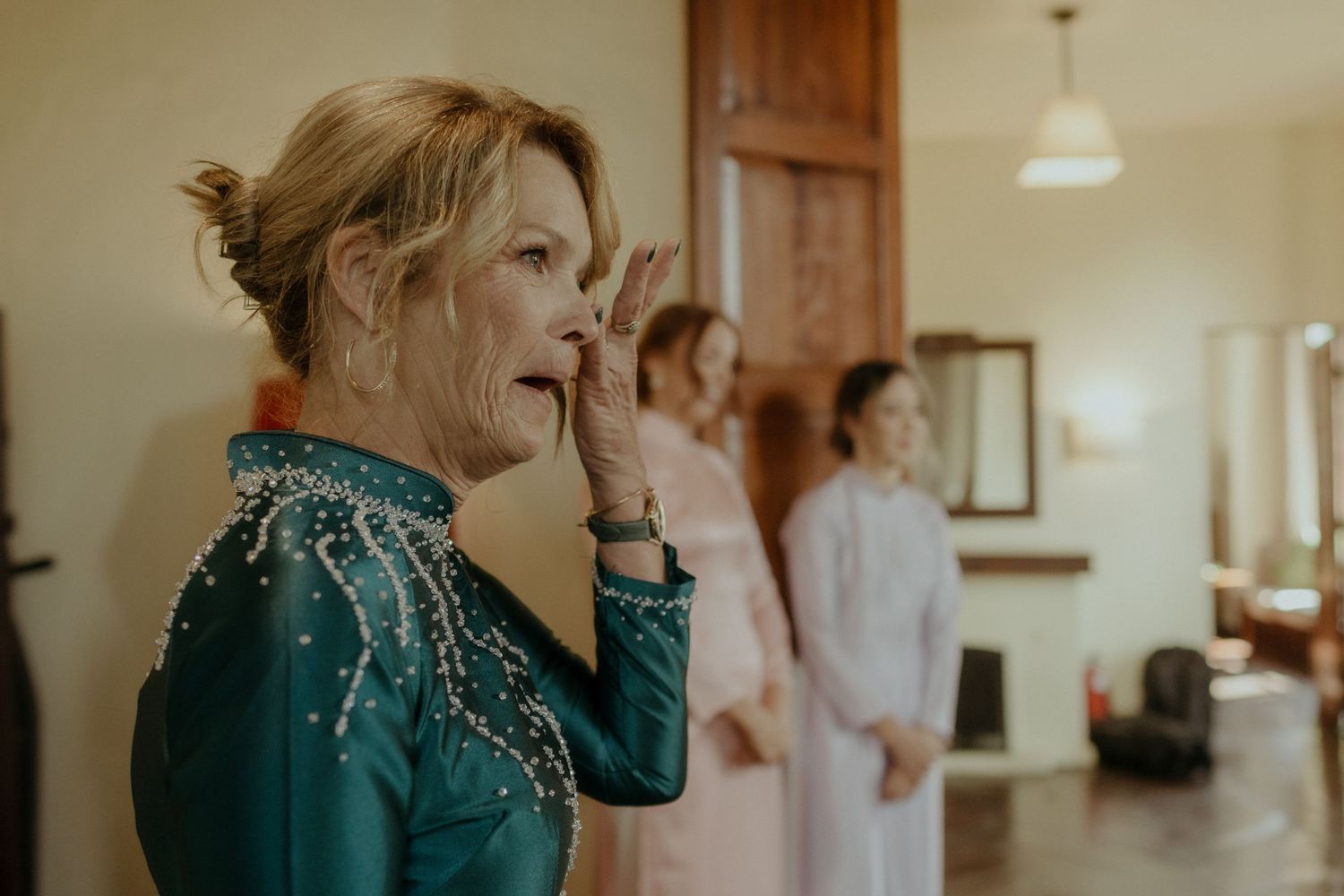 A person in a sparkly teal dress gasps with excitement while getting ready in a sunlit room with others.