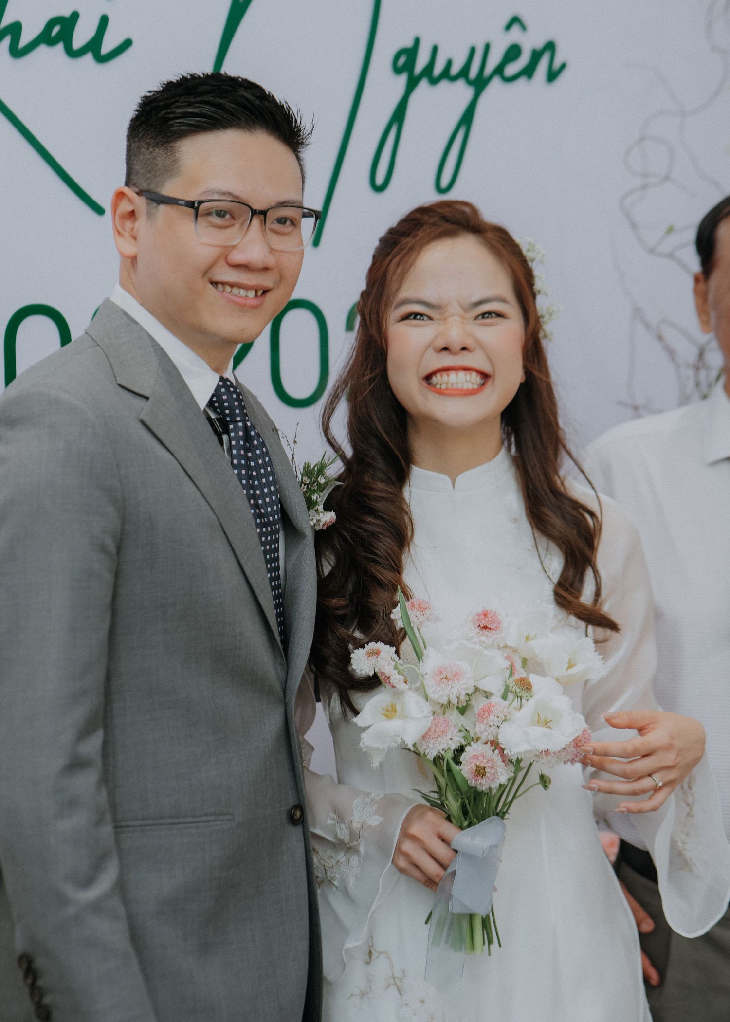 A wedding couple poses together with the bride holding a pastel bouquet while wearing traditional Vietnamese ao dai.