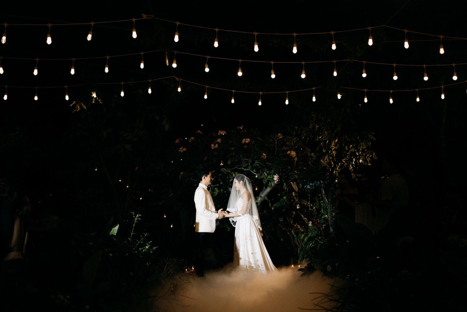 Silhouetted couple under string lights in nighttime garden setting.