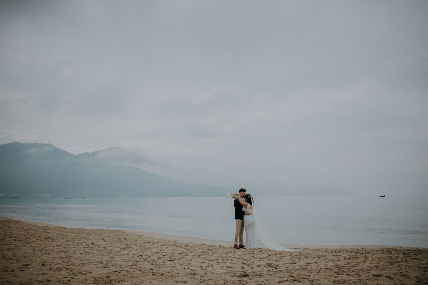 Distant silhouette of a person standing on a beach with mountains in the background.