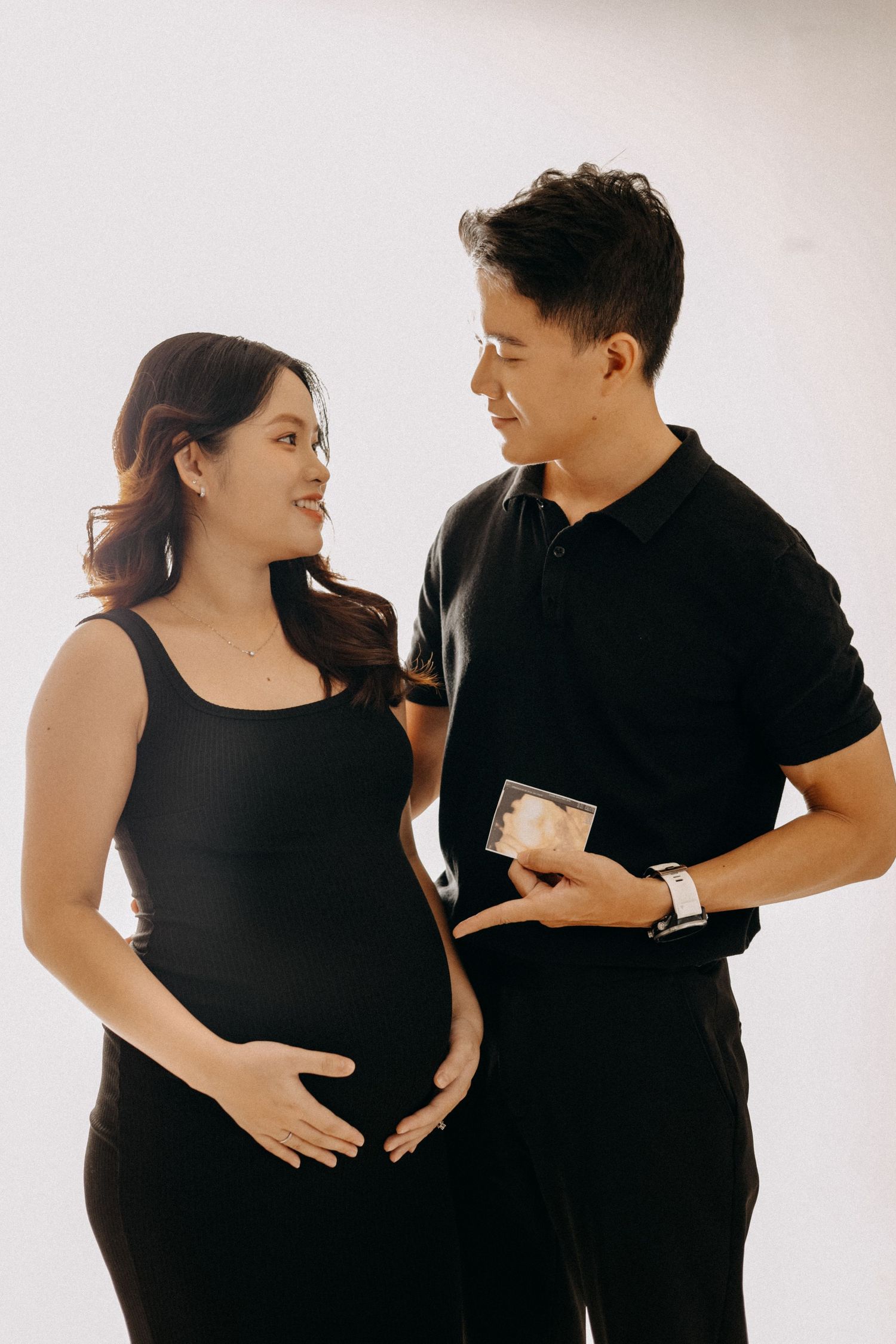 A couple in matching black outfits shares a tender moment during their pregnancy photoshoot.