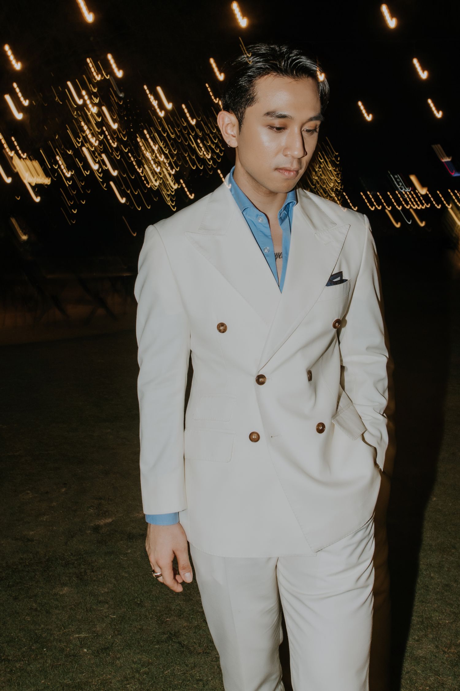 A stylish portrait featuring a white double-breasted suit against a backdrop of glowing lights.