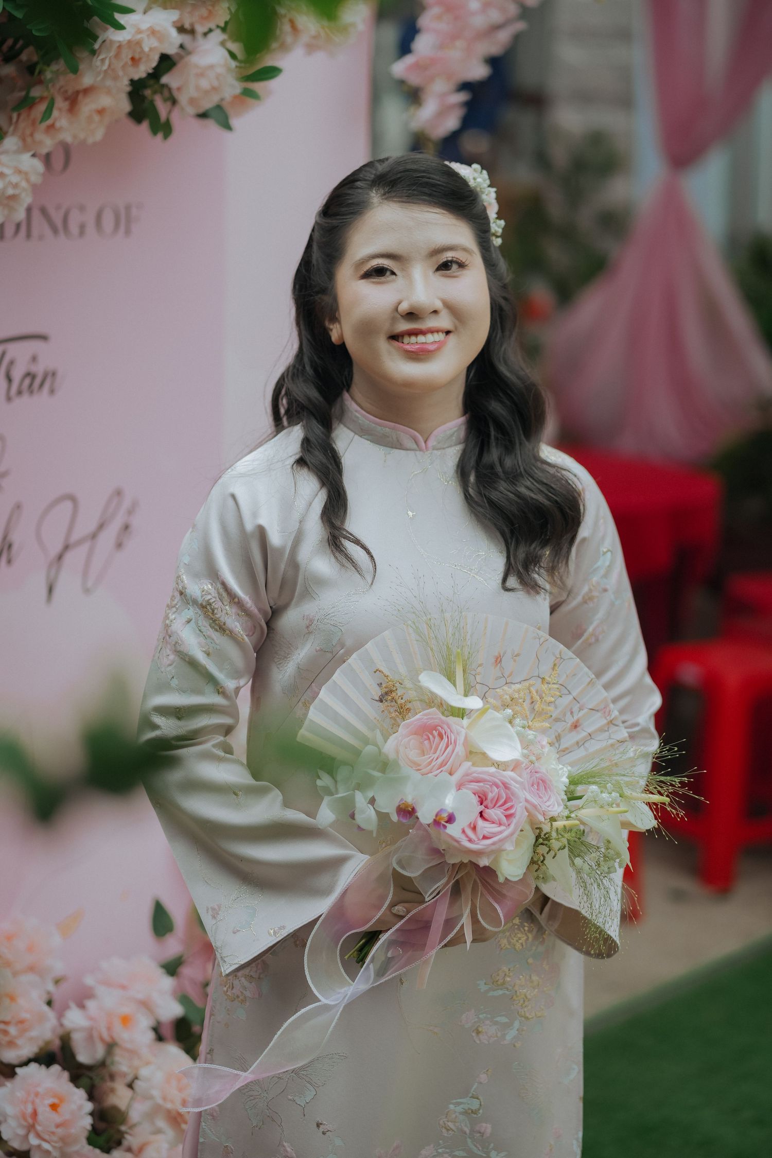 Traditional Vietnamese wedding ceremony with elegant bride in ao dai holding pink and white floral bouquet.