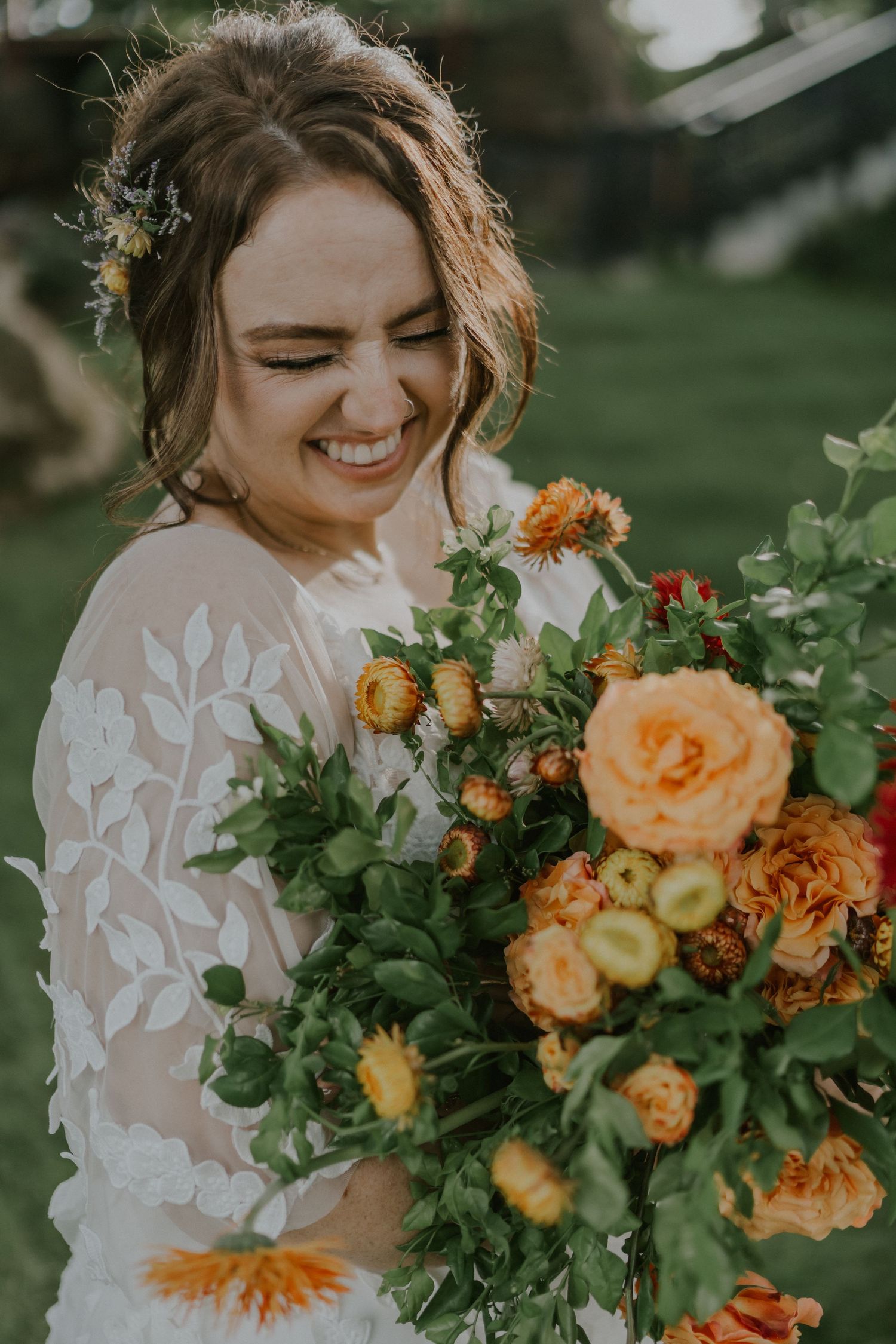 Bride laughs while holding vibrant orange and yellow floral bouquet outdoors.
