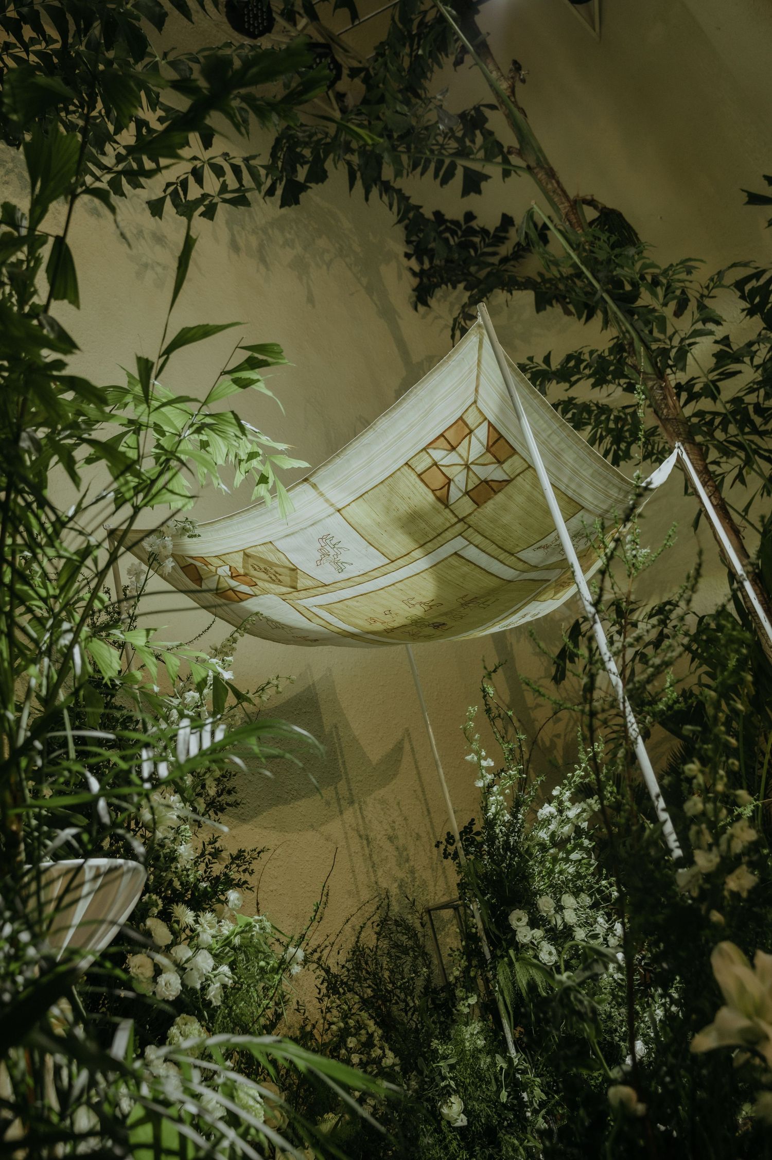 White ceremonial canopy draped among indoor greenery and foliage for a wedding.