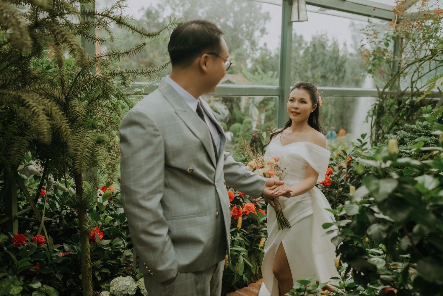 A romantic wedding photography session inside a lush greenhouse with red flowers and greenery.