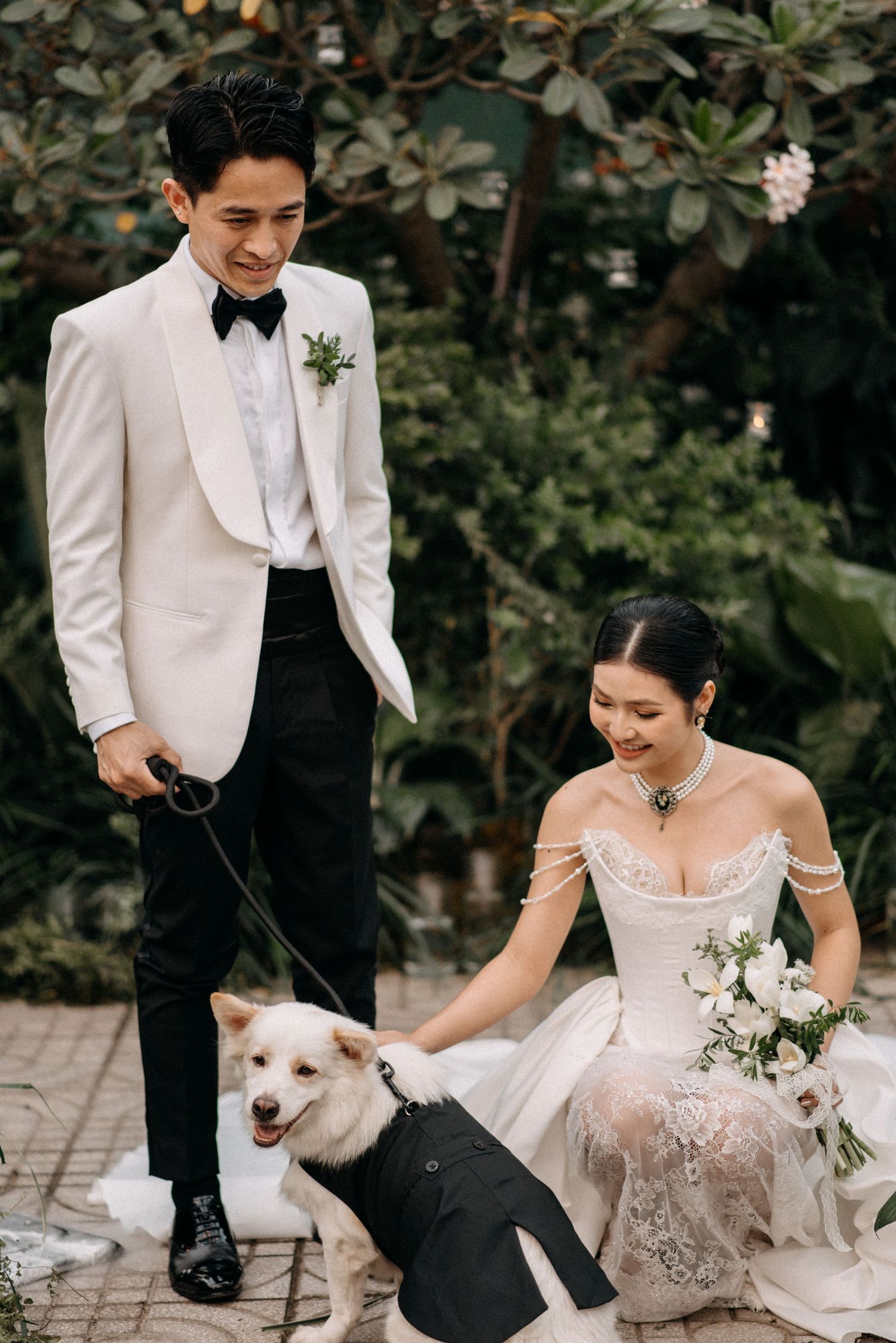 Wedding couple in white attire posing with their dog wearing formal black attire.