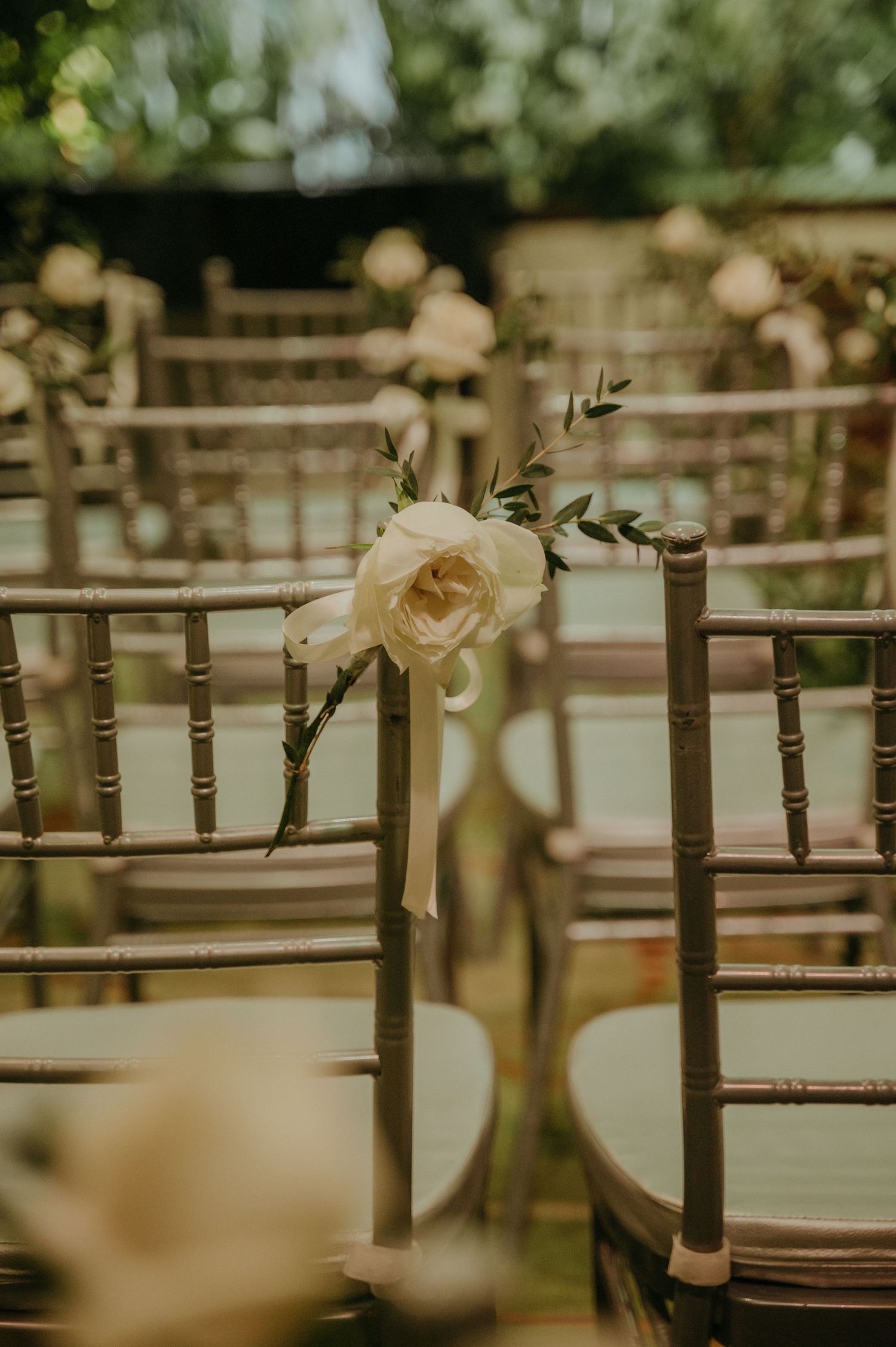 Single white rose decorating a Chiavari chair at an outdoor wedding ceremony.