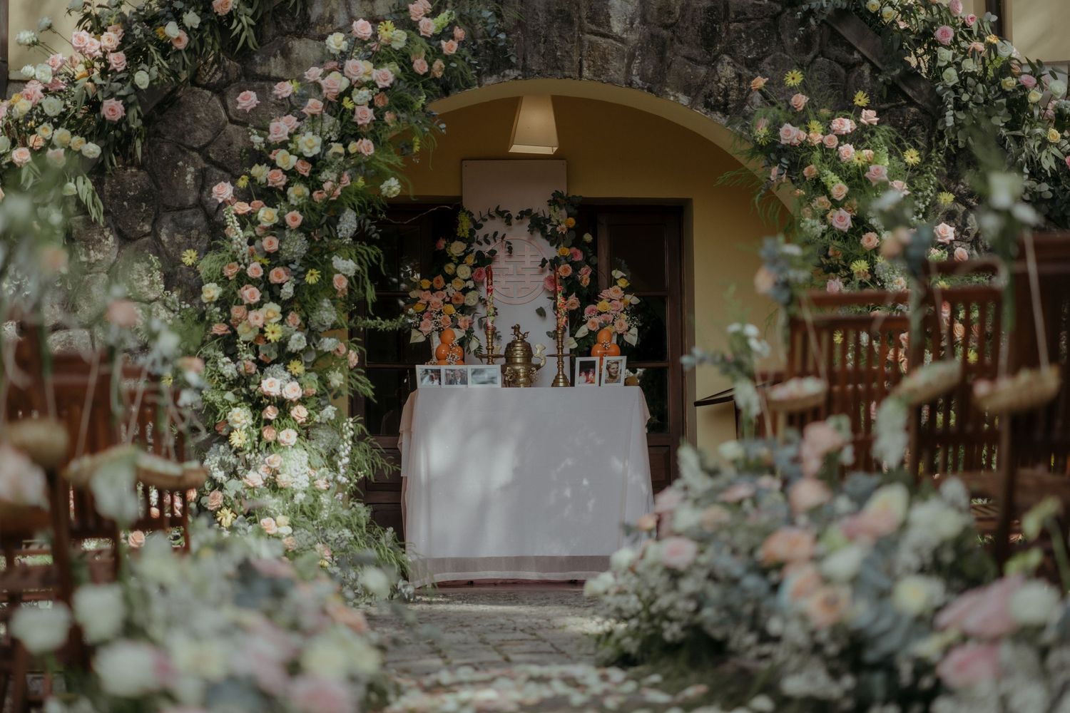Romantic garden wedding bar setup with floral arch and white roses decorating a stone archway entrance.