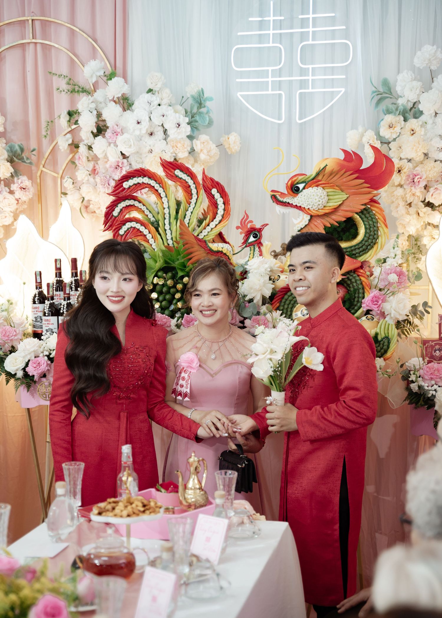A traditional Chinese wedding celebration with red and pink decor featuring ornate phoenix and dragon decorations and floral arrangements.