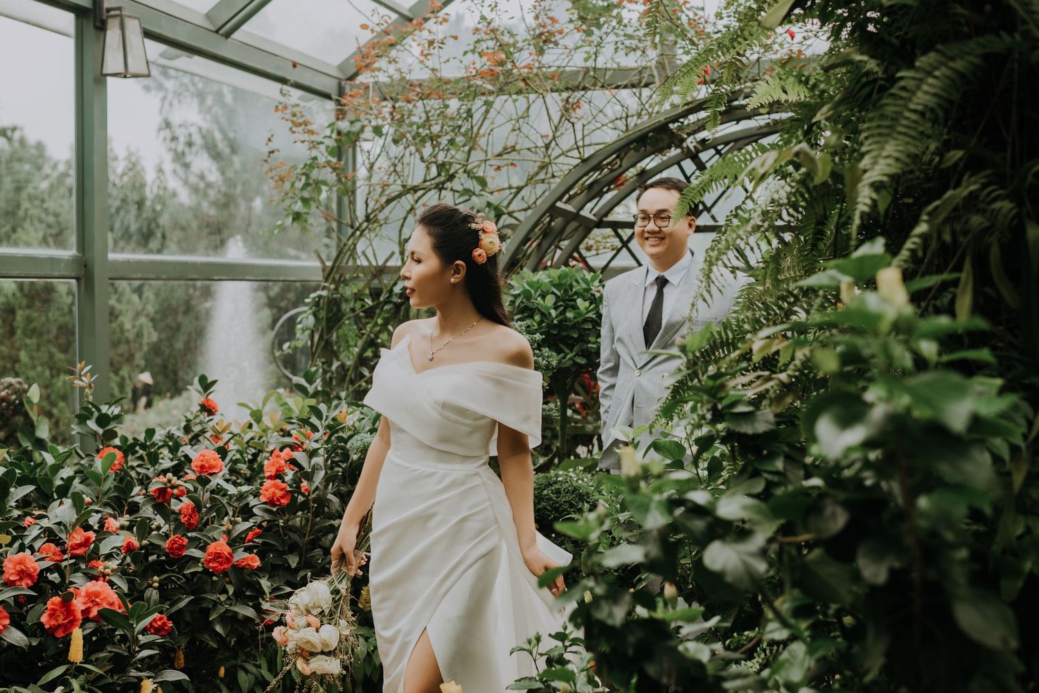 A couple shares a romantic moment in a lush greenhouse filled with tropical plants.