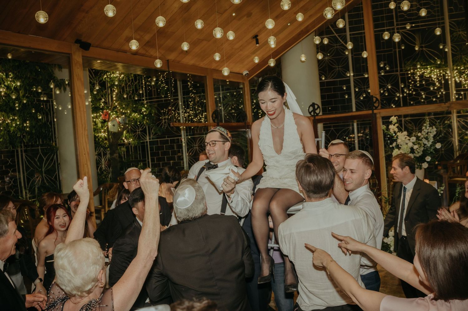 Wedding party lifts guests during an energetic dance celebration under twinkling lights.