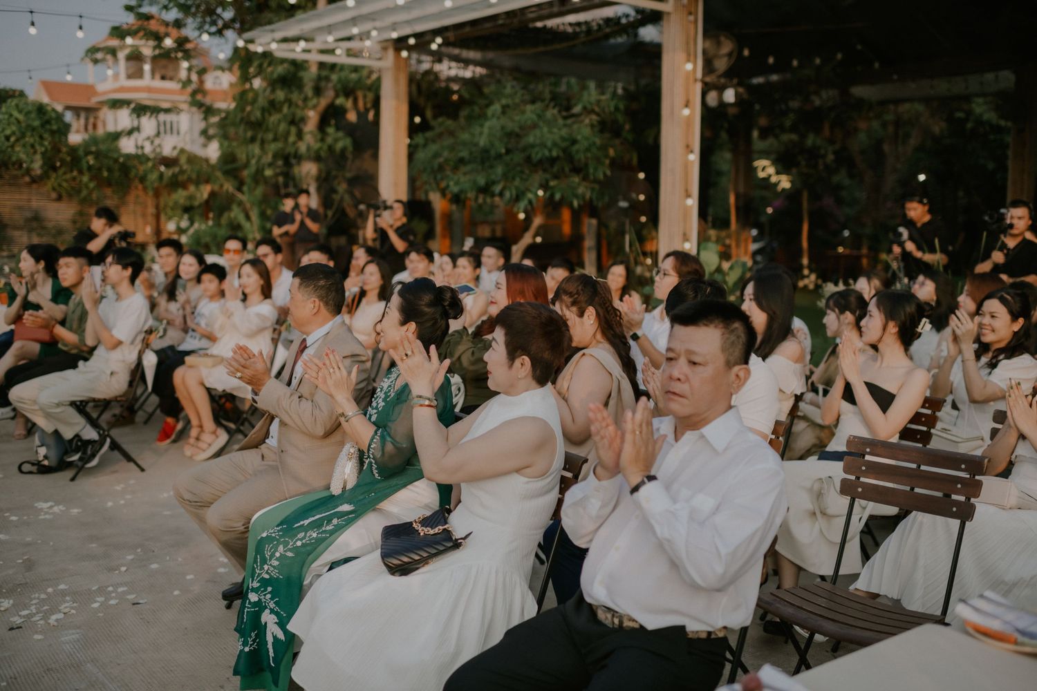 Wedding ceremony guests seated outdoors under string lights at dusk during an intimate celebration.