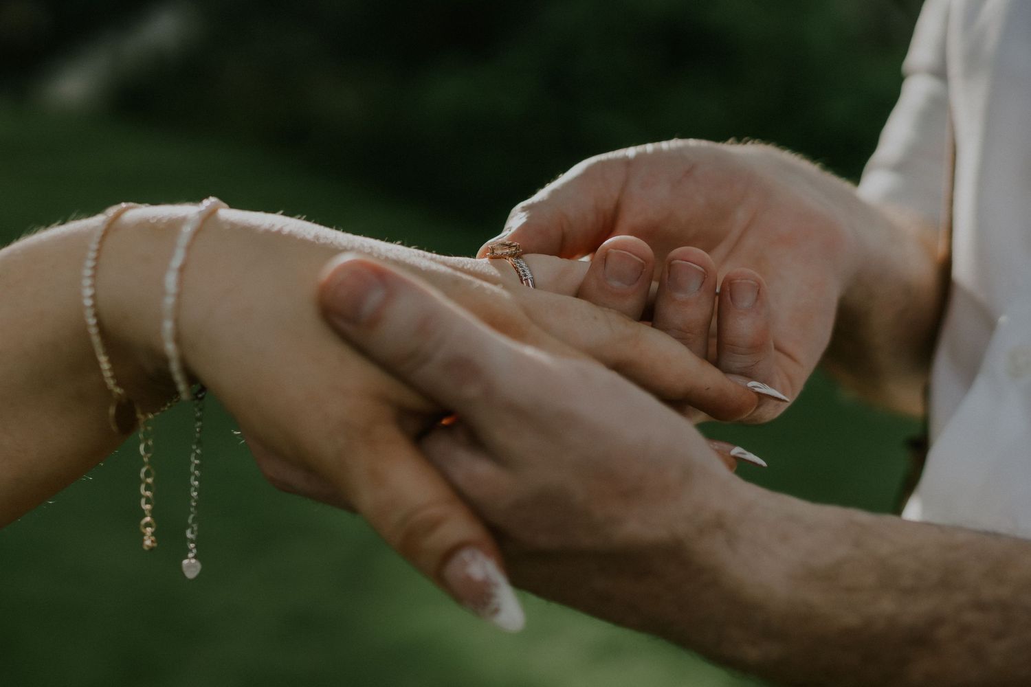 Close-up of hands exchanging wedding rings during outdoor ceremony.