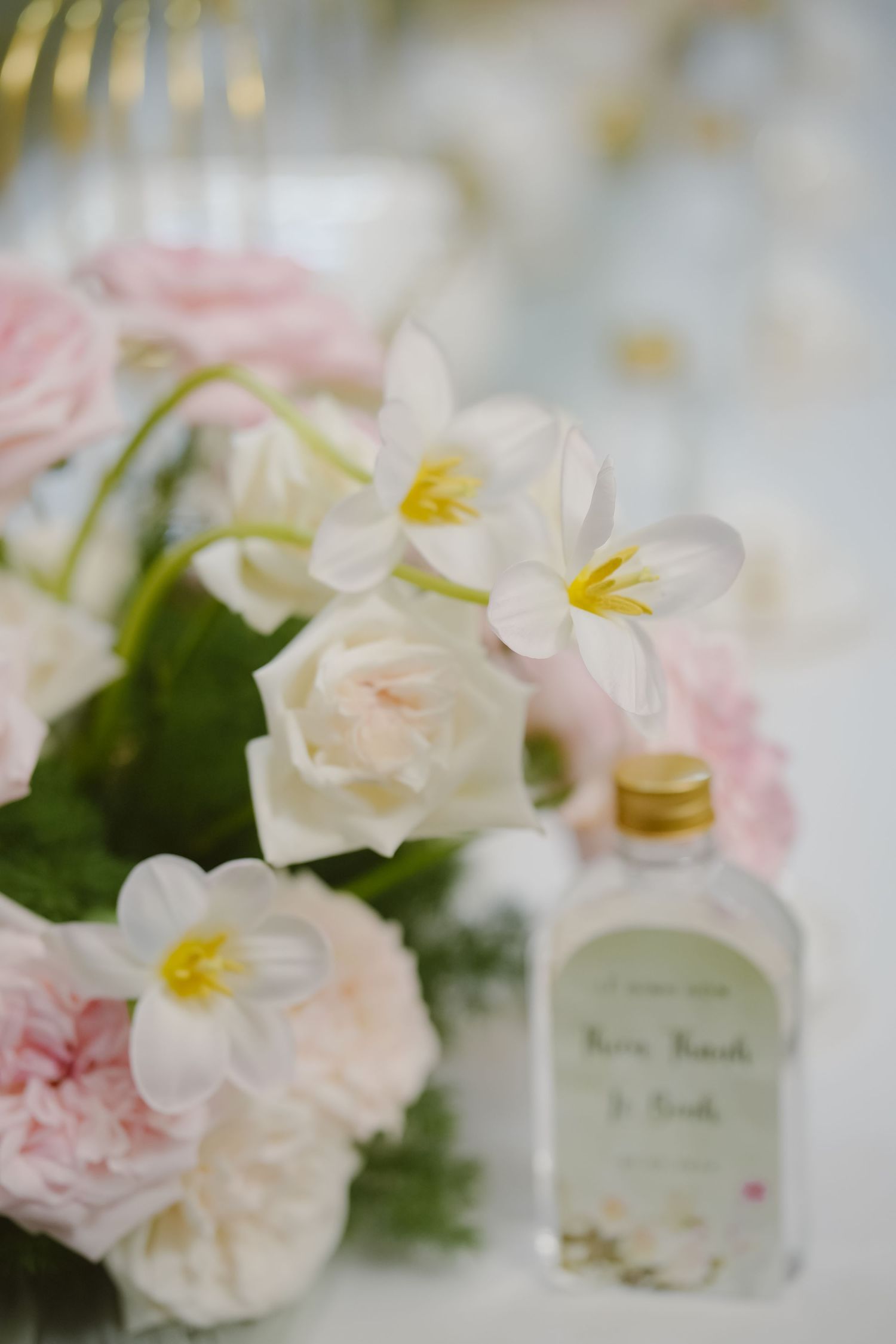 Delicate pink roses and white flowers arranged with a decorative bottle on a table.