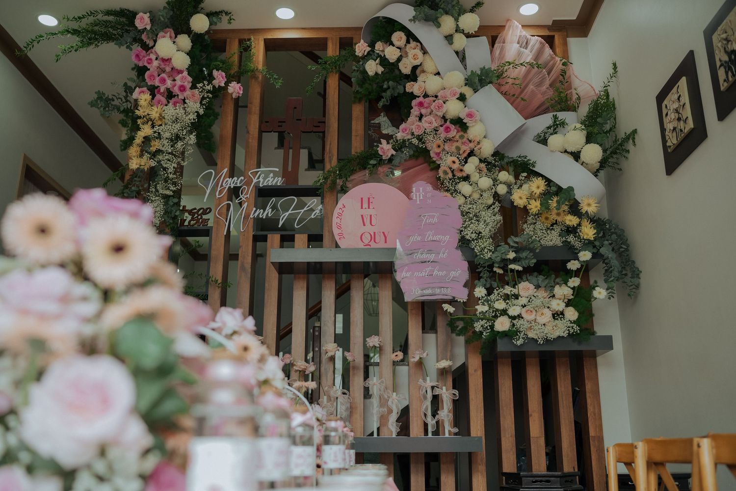 Pink and white floral arrangements adorn a wooden slatted wall with hanging lanterns.