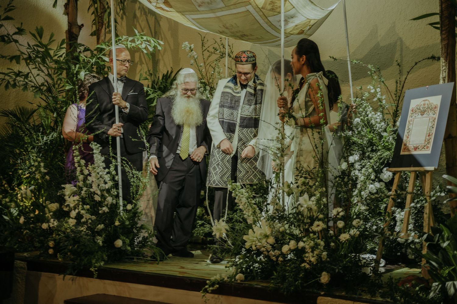 Wedding party gathered on a decorated stage with abundant floral arrangements and natural elements.