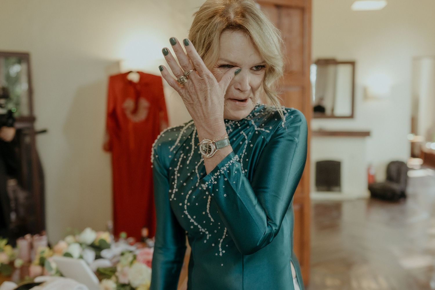 A person wearing a teal sequined dress expresses emotion by covering their face with their hand in an indoor setting.