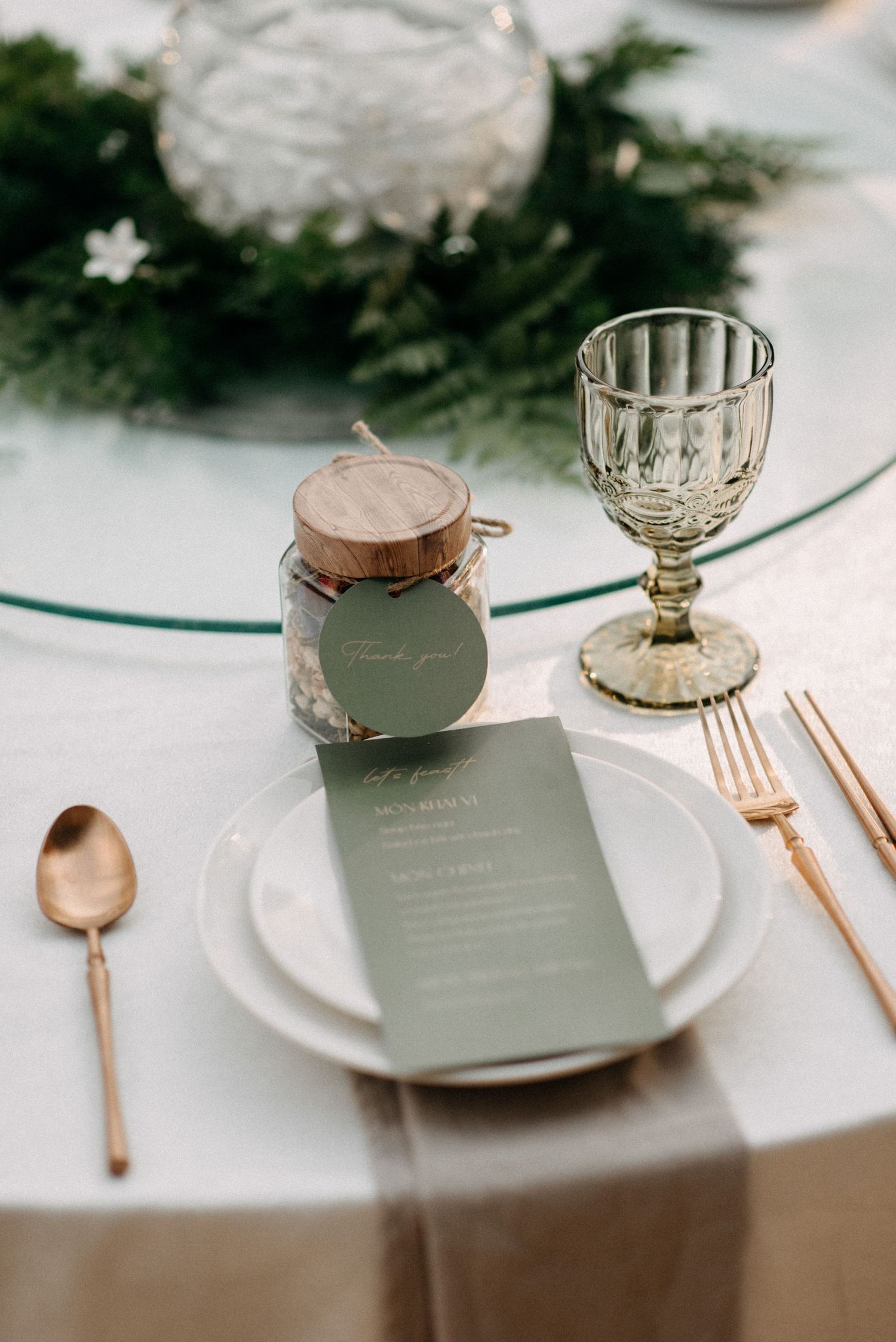 Elegant table setting with crystal glass, gold cutlery, and green menu card on white plate.