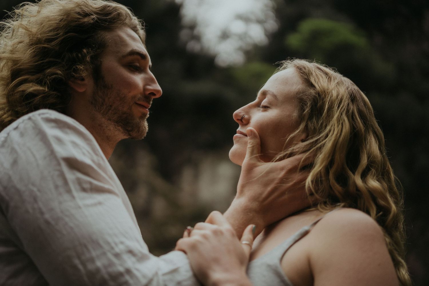 A tender romantic moment captured between a couple in an intimate embrace against a dark natural backdrop.