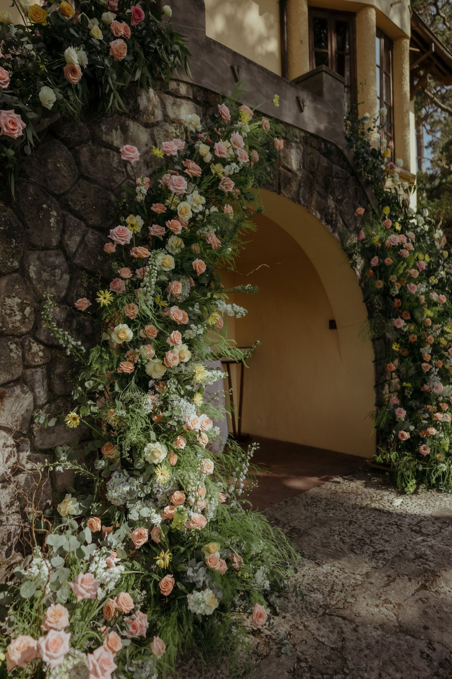 Lush pink climbing roses adorn a stone archway entrance with Mediterranean architectural details.