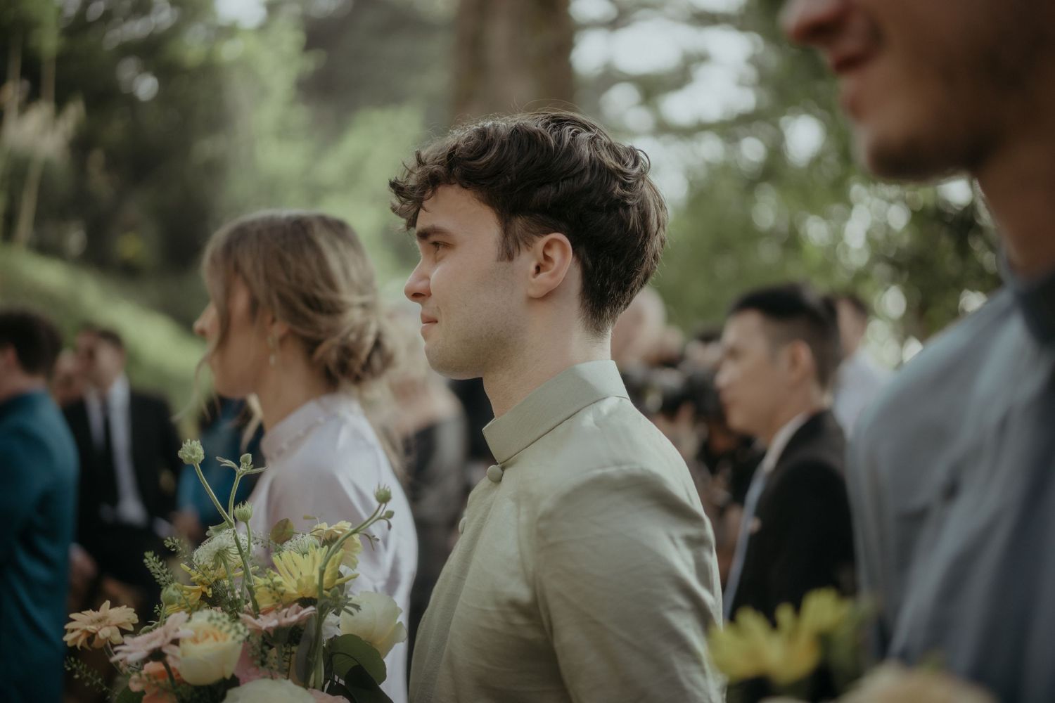 Attendees stand together at an outdoor wedding ceremony with natural greenery in the background.