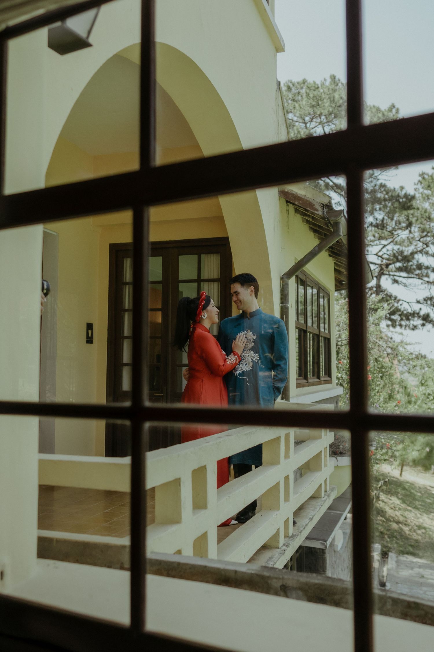 A couple stands on a porch having a conversation, viewed through a windowpane with dark grid lines.