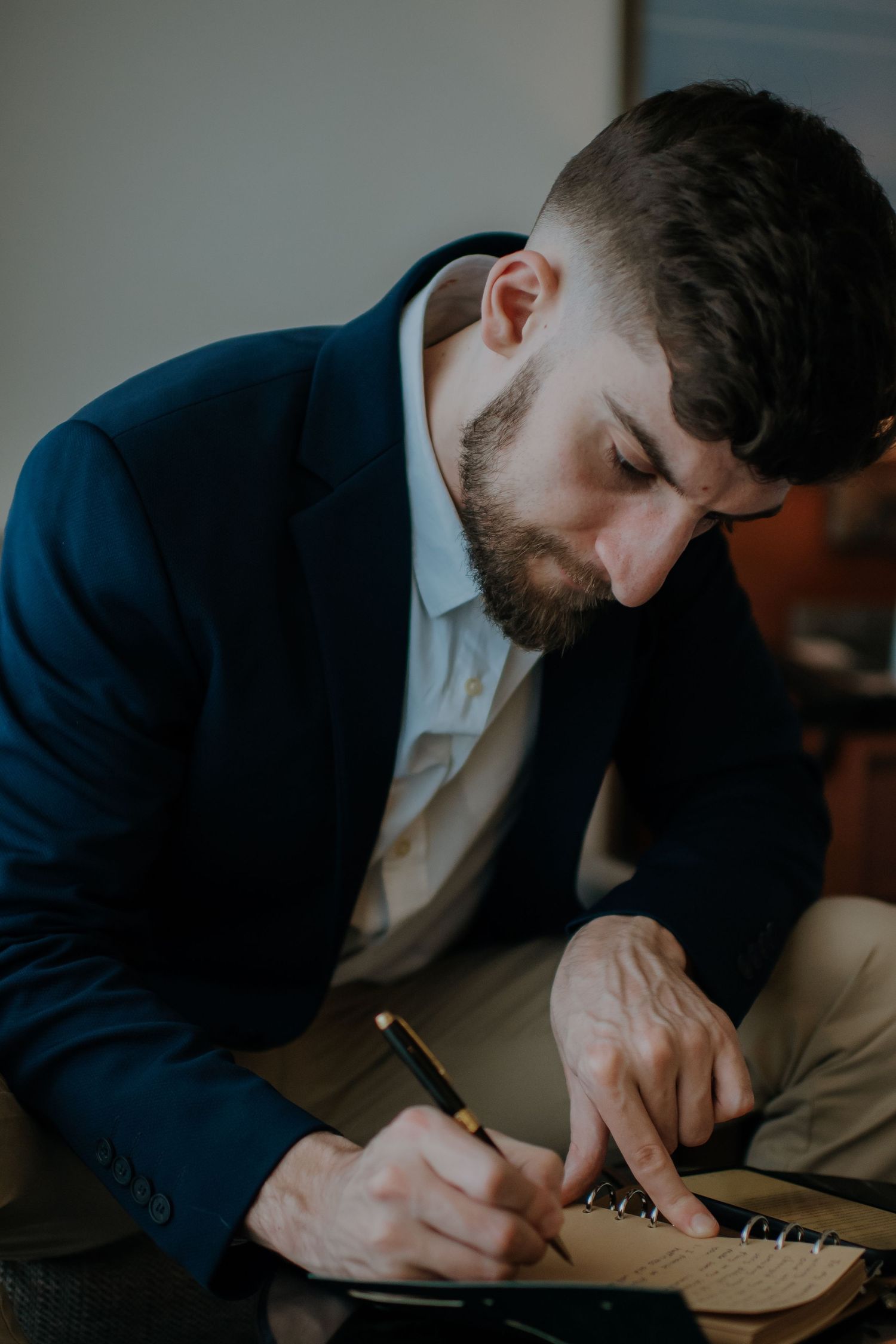 Person in navy suit writing in notebook with focused concentration.