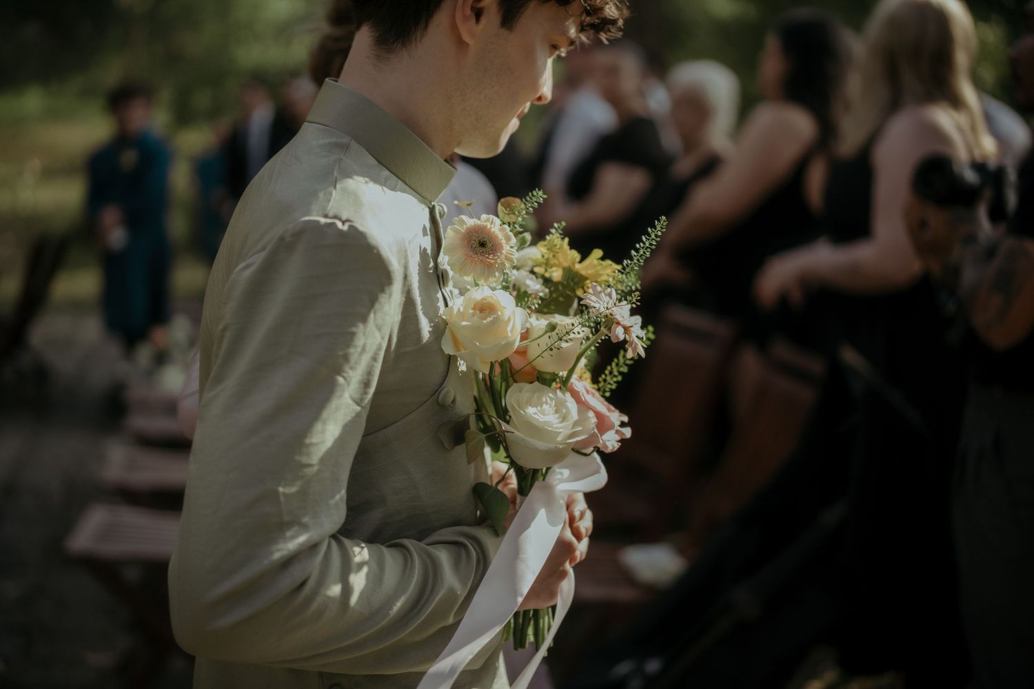 Soft pink and white floral wedding bouquet held against light colored formal wear at an outdoor ceremony.