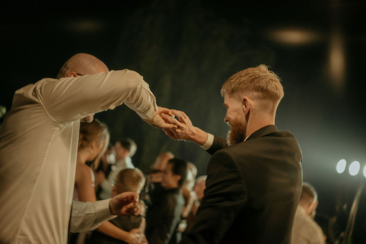 An enthusiastic crowd dancing and celebrating at a dimly lit indoor event with blurred lights in the background.
