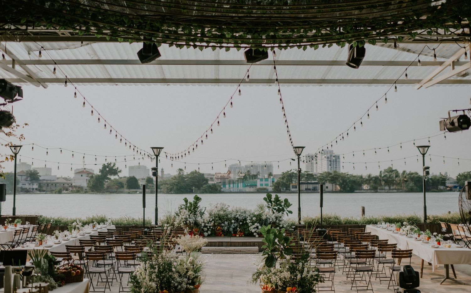 Outdoor wedding venue setup with string lights and white chairs overlooking a waterfront view.