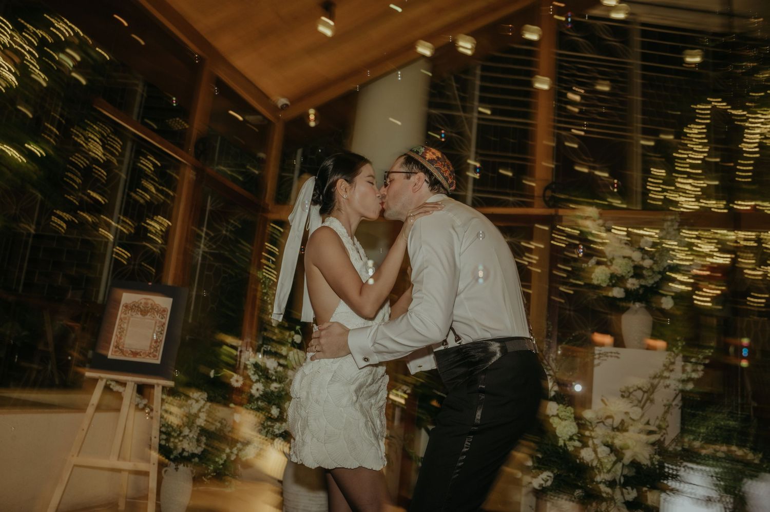 Couple sharing a romantic kiss during their wedding dance under shimmering lights.