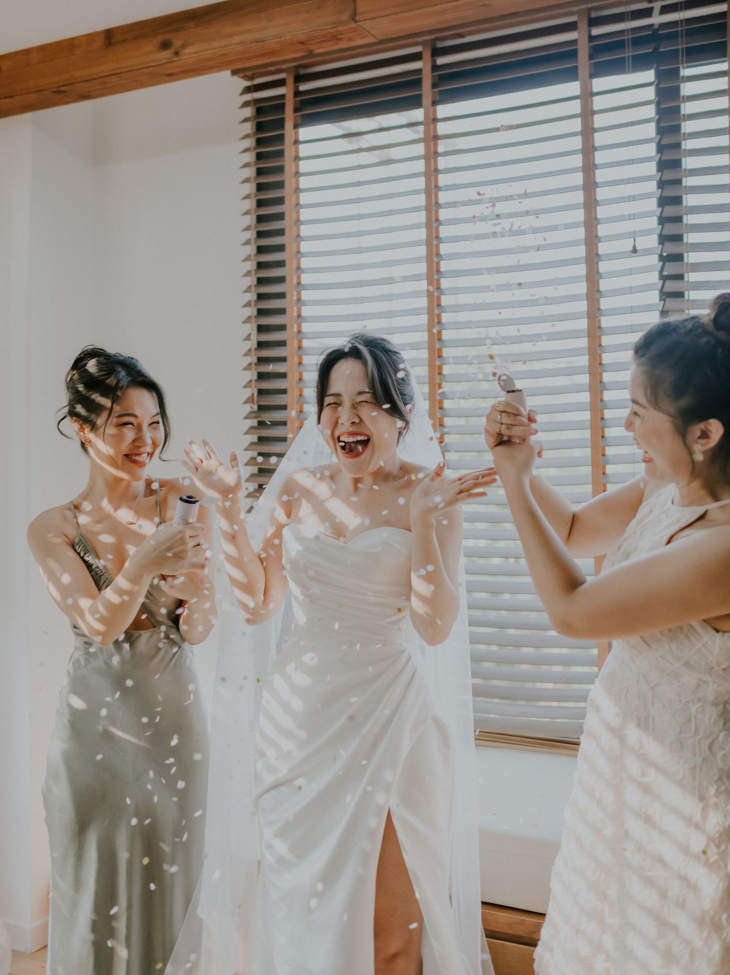 Celebration with confetti during wedding preparations in front of window with venetian blinds.