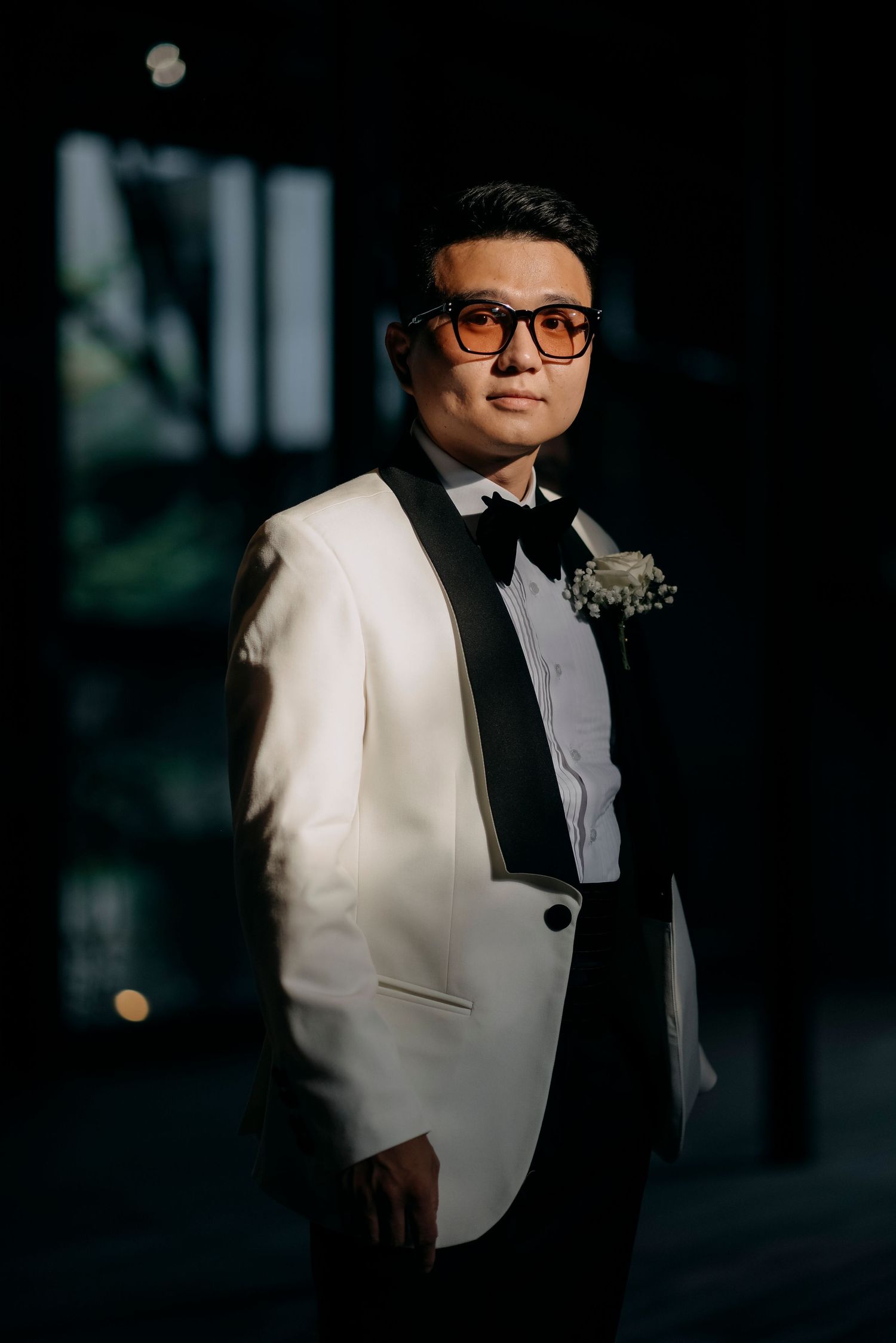 Elegant groom poses in white tuxedo jacket and black bow tie.