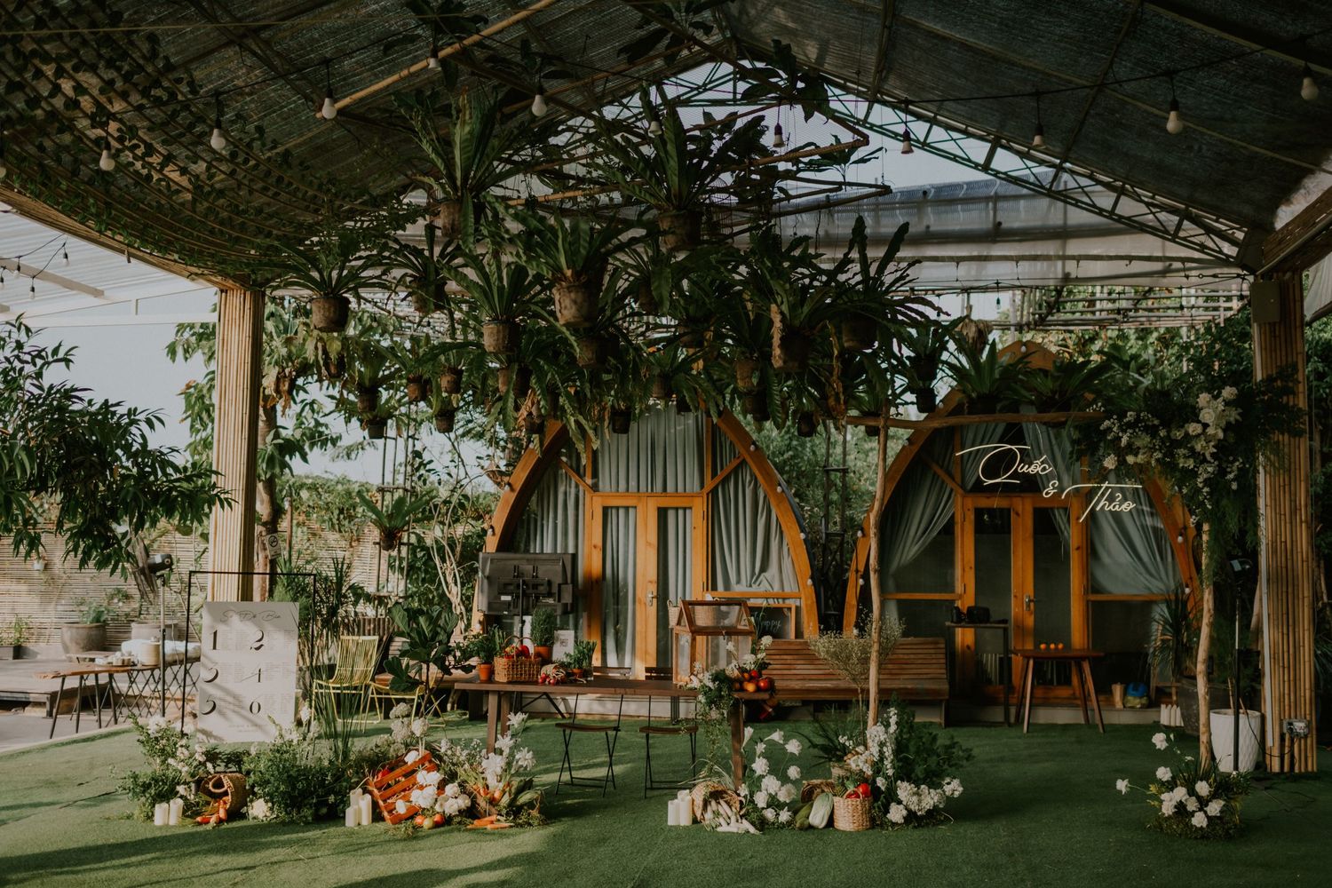 Indoor greenhouse venue decorated with hanging plants and floral arrangements for an event.